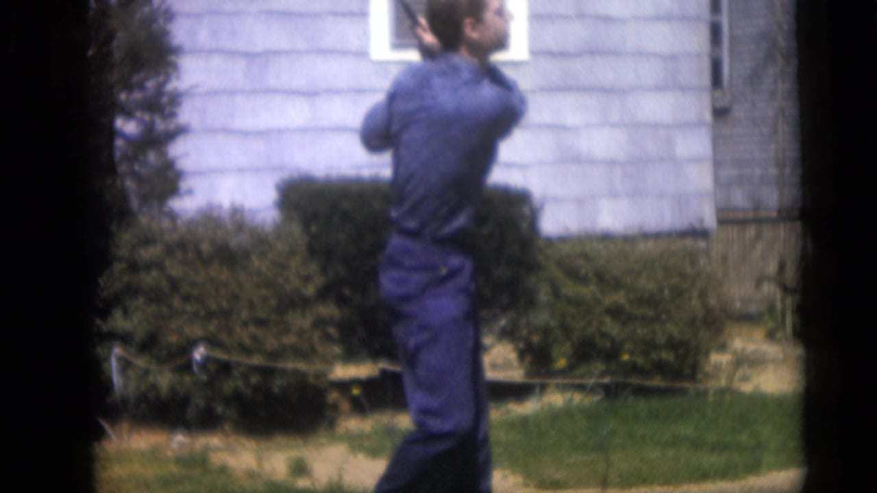 1959 Camden, New Jersey home-movie frame showing a man mid-swing with a golf club near shrubs and a light-colored house.