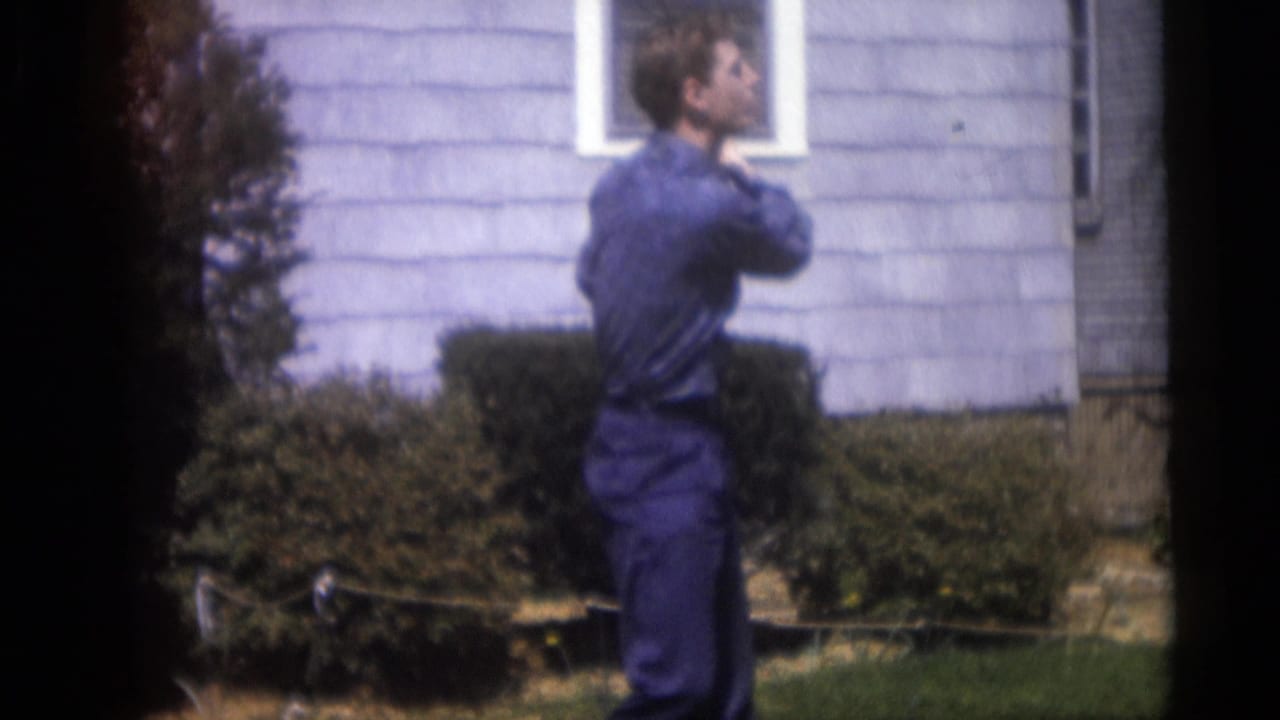 Man holds a golf club near his shoulder while standing in front of a house.