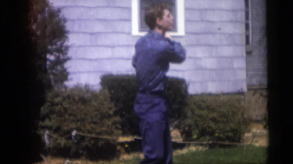The man appears in profile with a golf club raised near his shoulder outside a Camden home in the 1959 footage.
