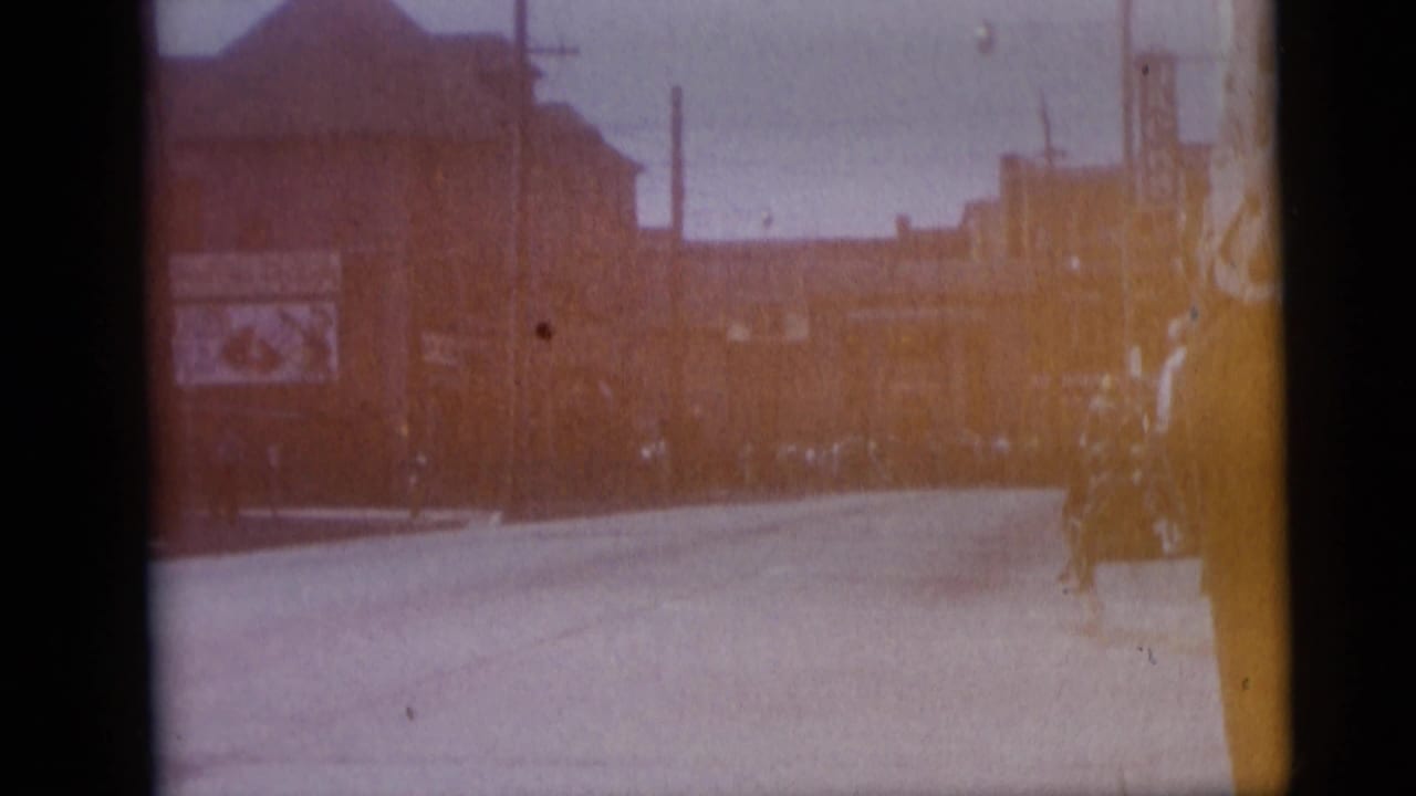 1959 Camden, New Jersey street view with a broad road, commercial buildings, billboard, poles, and distant pedestrians or vehicles.