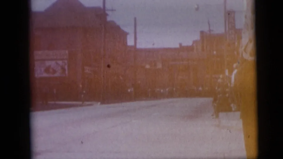 1959 Camden, New Jersey street view with a broad road, commercial buildings, billboard, poles, and distant pedestrians or vehicles.