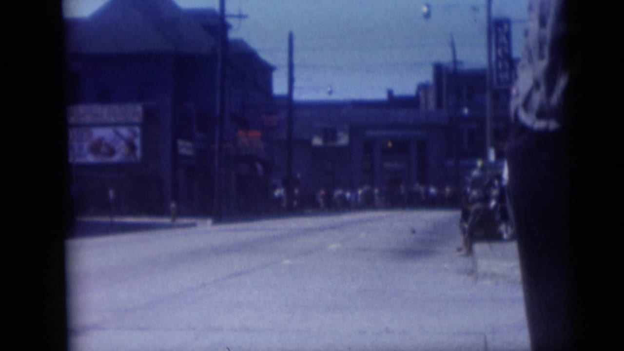 Camden, New Jersey street scene from 1959 showing a broad road, storefront block, utility poles, distant pedestrians, and a dark foreground figure.