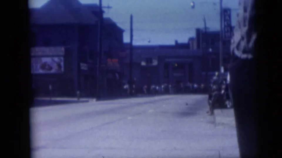 Camden, New Jersey street scene from 1959 showing a broad road, storefront block, utility poles, distant pedestrians, and a dark foreground figure.