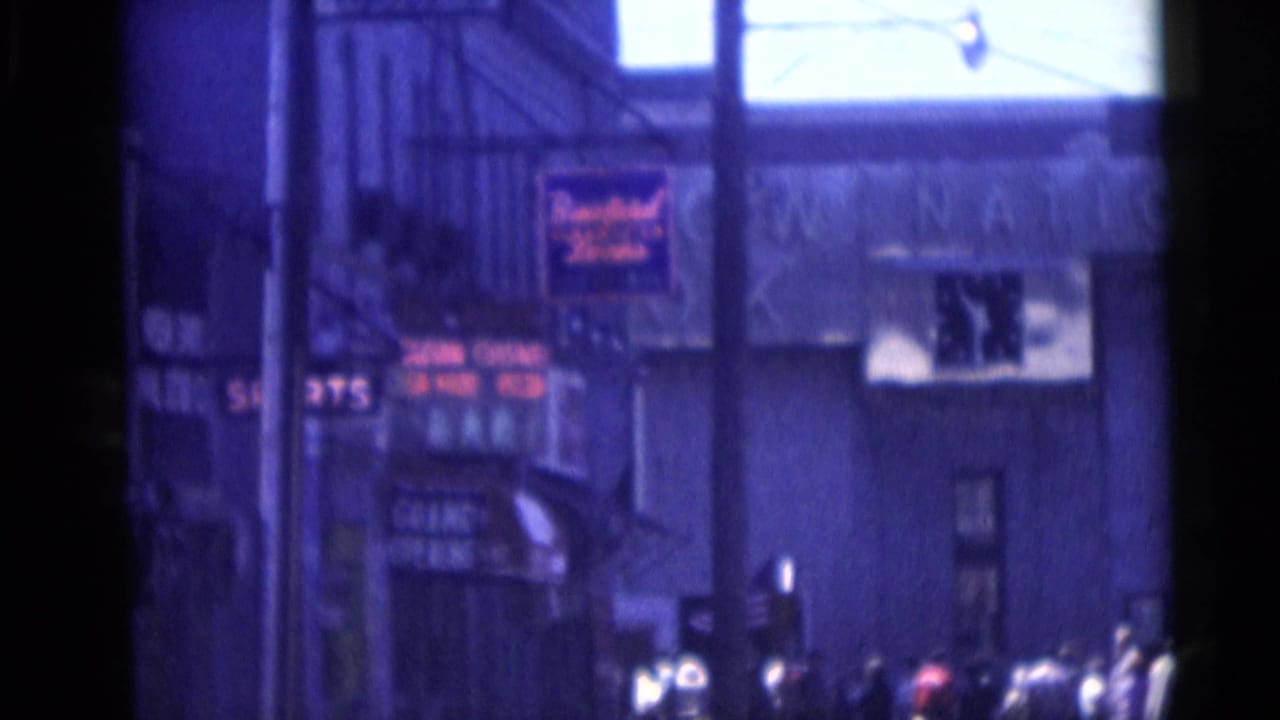 Street-side view of storefront signage and spectators near a parade route.