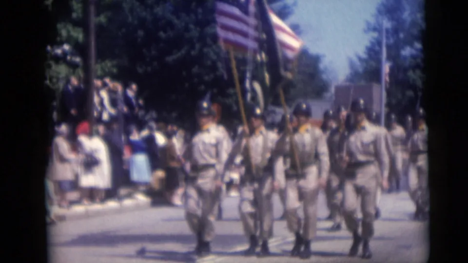 1959 Camden parade footage shows soldiers in uniform approaching the camera with an American flag and spectators at the curb.
