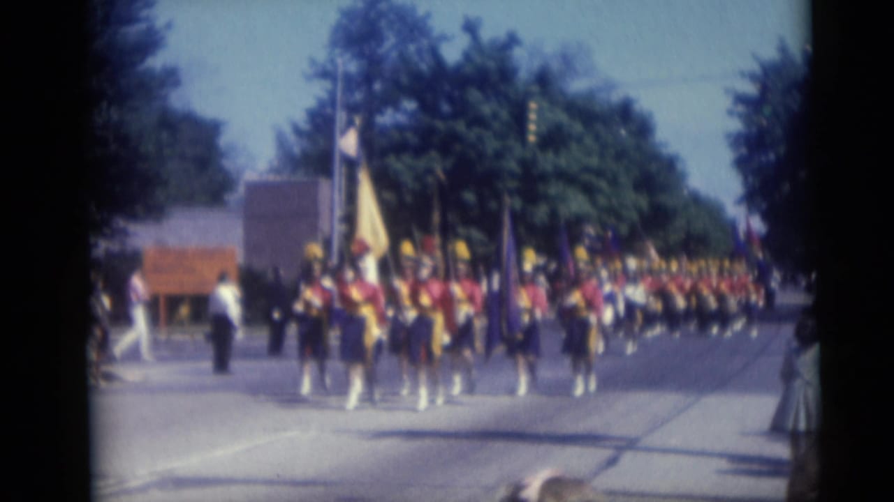 A color guard carrying flags leads a marching band in red and blue uniforms during the 1959 Camden parade.
