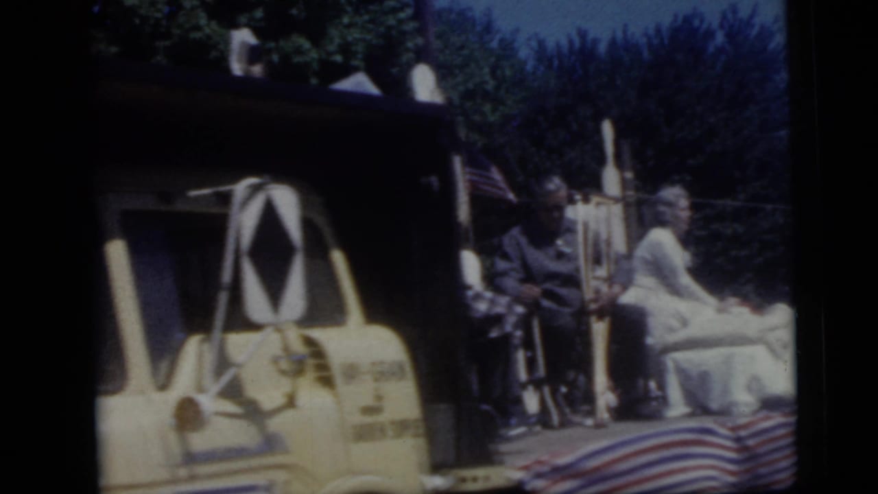 A closer side view of the yellow parade truck shows seated or posed figures, flags, and striped fabric along the lower frame.