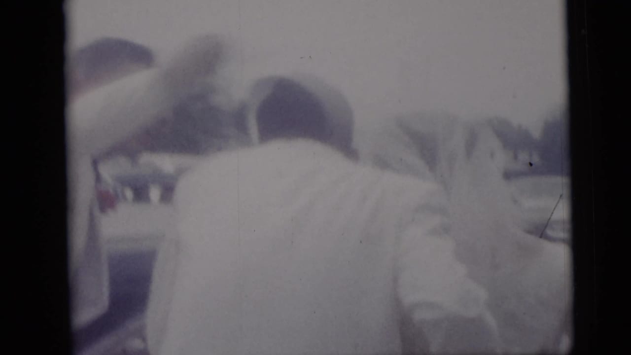 Rear view of people in light clothing gathered beside a car.