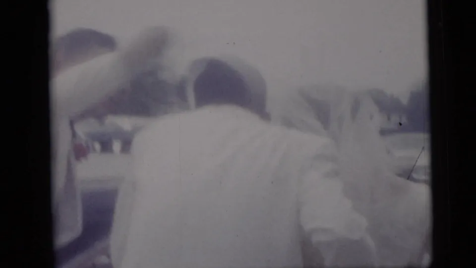 Rear view of wedding participants in light clothing near a car, filmed in Camden, New Jersey, in soft 1959 8mm color.