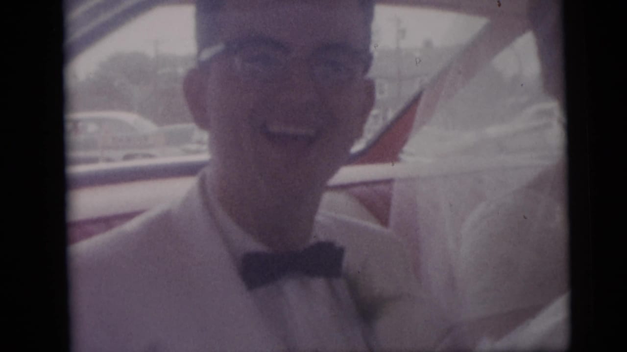 Smiling groom in a light suit and bow tie stands beside a bride in white during a 1959 Camden, New Jersey wedding home movie.