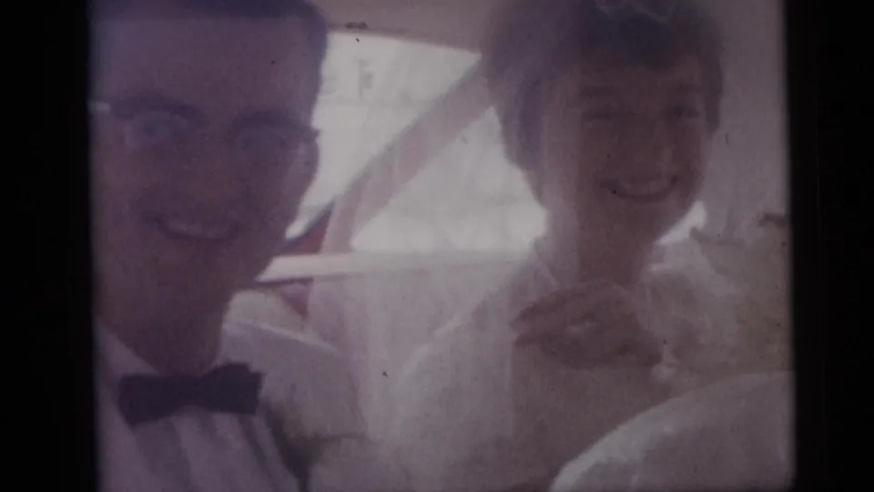 In Camden, New Jersey, 1959, a bride and groom smile from inside a wedding car as the camera looks through the window.