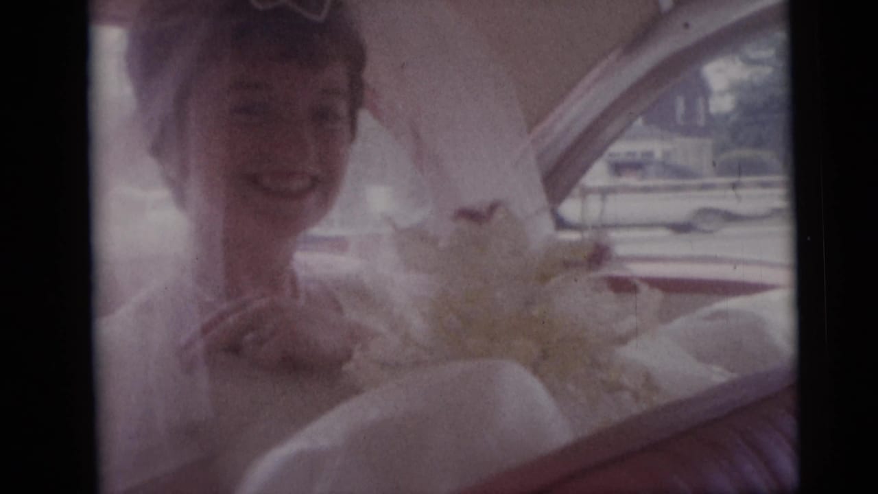 Bride smiling in a veil beside a bouquet inside the car.