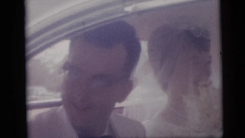 Newlywed couple in a 1959 Camden home movie, with the groom in glasses and the bride in her veil inside a car.