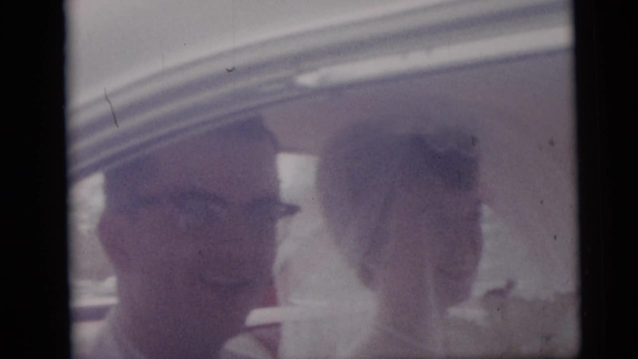 1959 Camden wedding footage frame with the bride and groom smiling inside a car, softened by aged 8mm color.