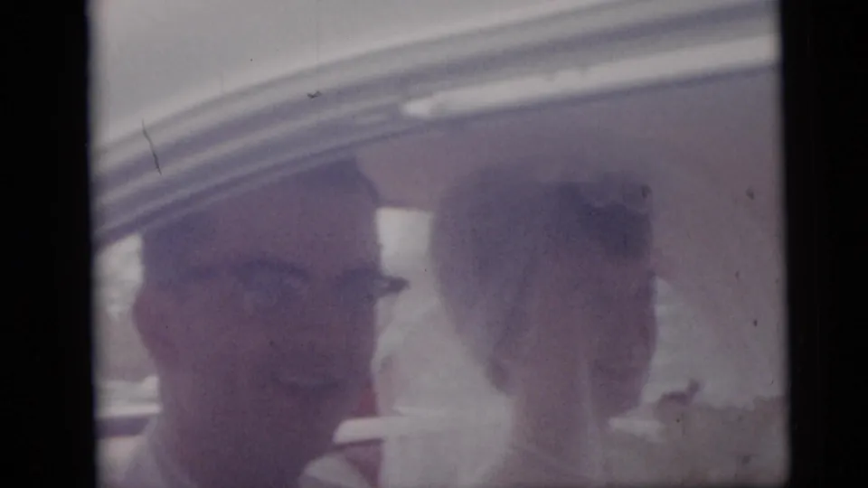 1959 Camden wedding footage frame with the bride and groom smiling inside a car, softened by aged 8mm color.