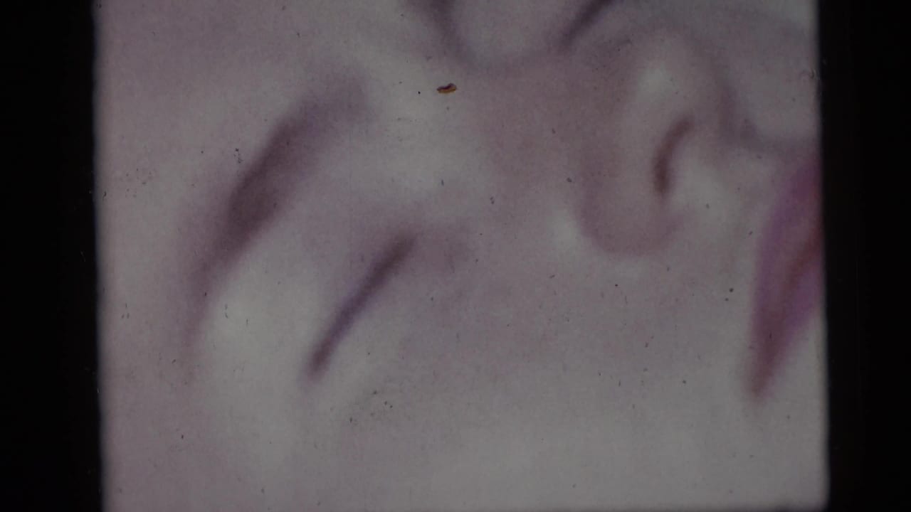 Soft 1959 Camden beach frame showing the resting girl’s face in close-up, with faded color and dust from the 8mm scan.