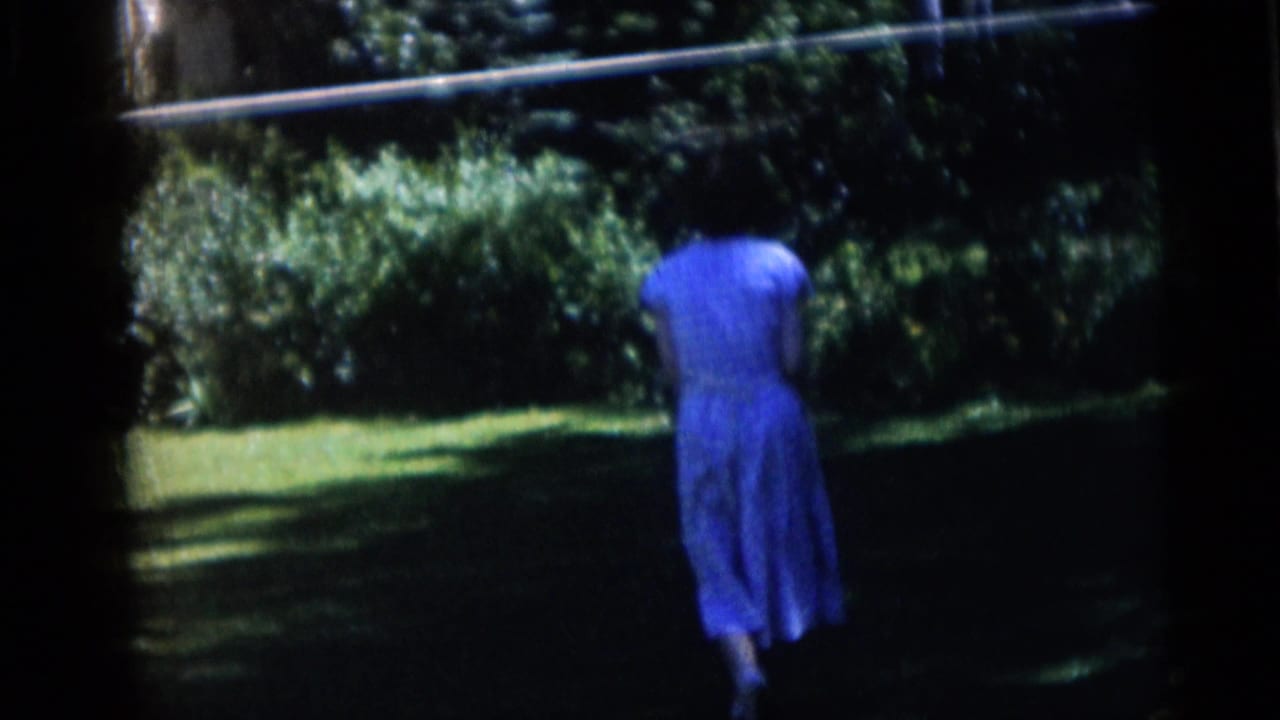 Woman in a blue dress walking away across a shaded grassy yard.
