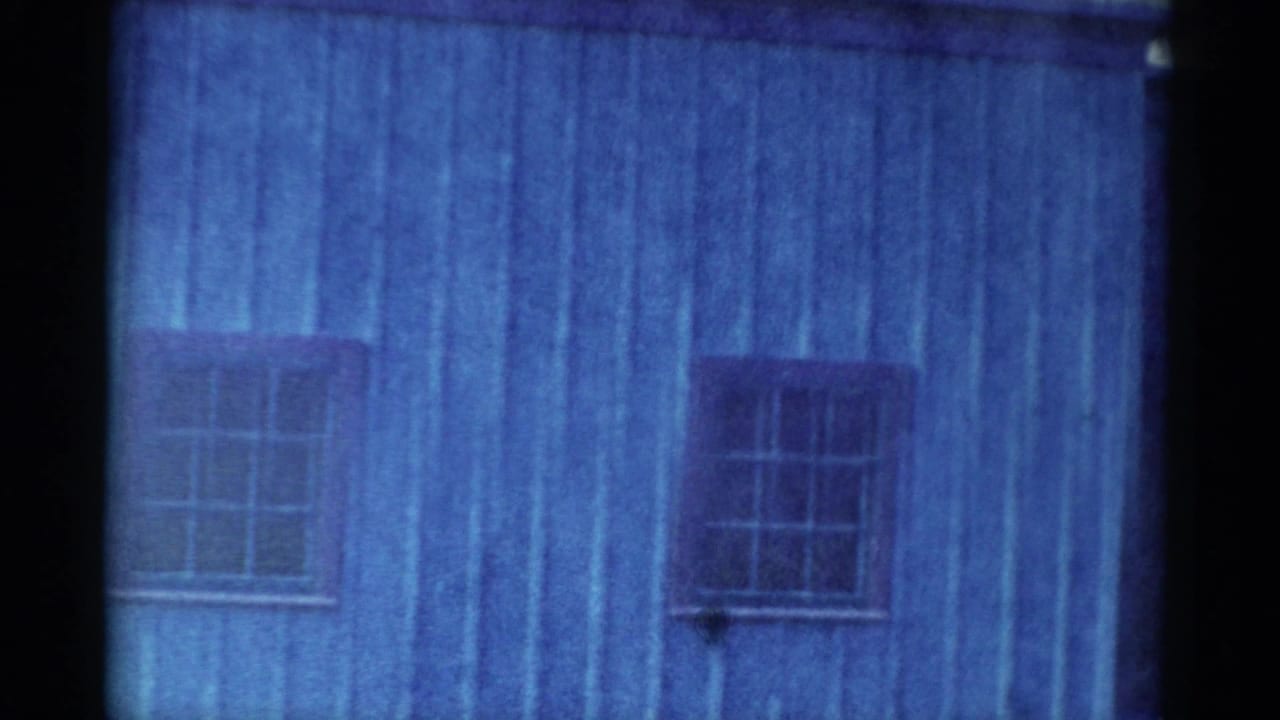 1959 Catskill-area 8mm frame showing weathered blue plank siding, a barred window, and a dark film divider at the right edge.