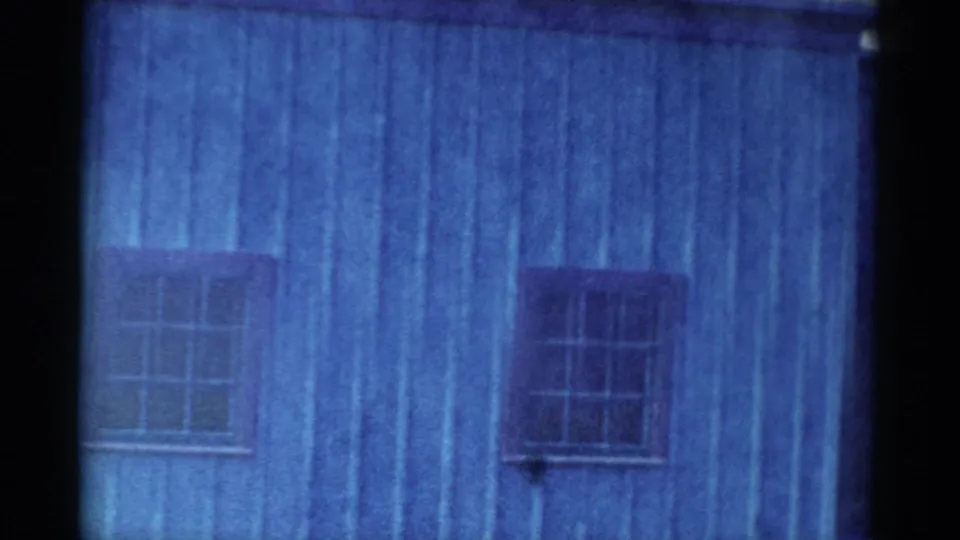 1959 Catskill-area 8mm frame showing weathered blue plank siding, a barred window, and a dark film divider at the right edge.