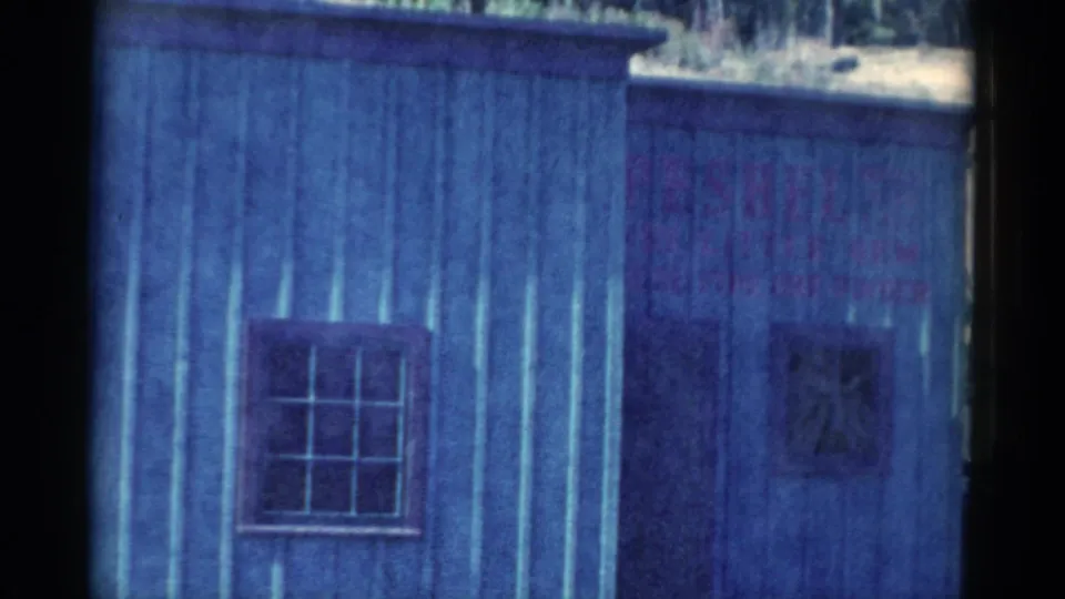1959 Catskill-area frame with a barred window on blue siding and a darker right-side opening or panel.