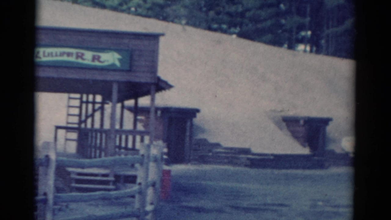 Wooden structure with a partially readable railroad-style sign beside a pale sloped embankment.