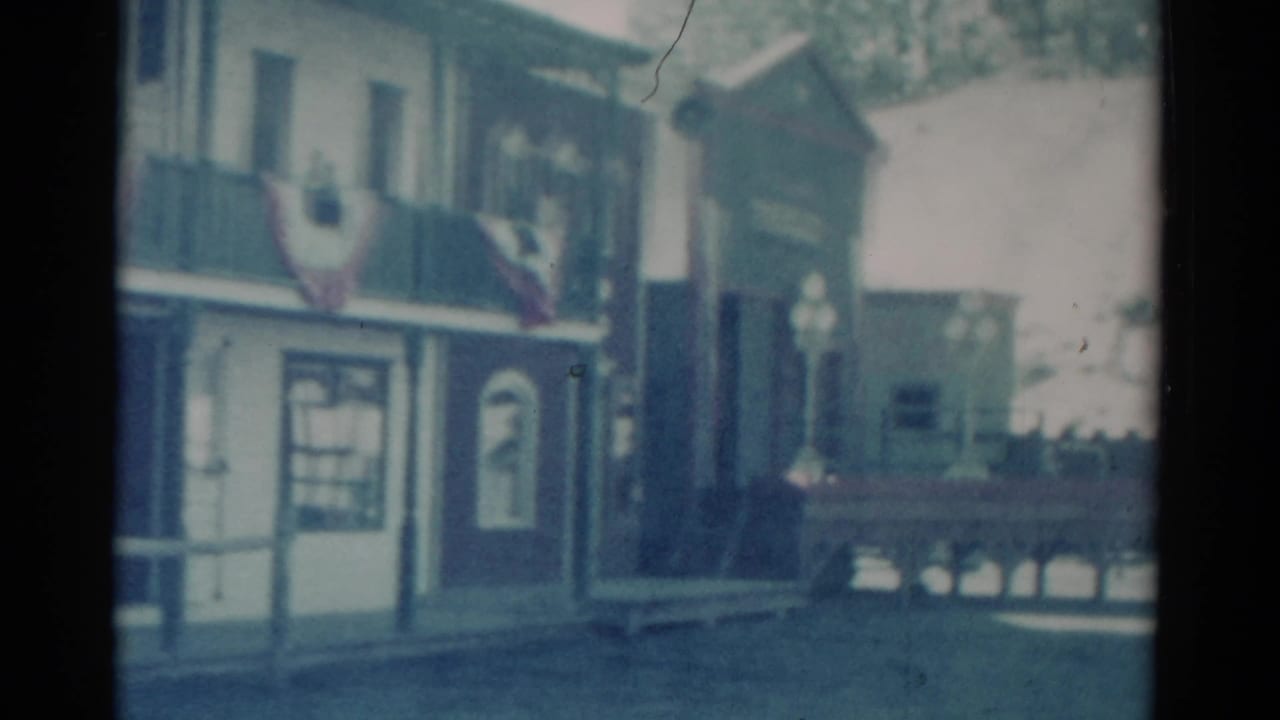 Small-town storefront with American flags beside a street and railing.