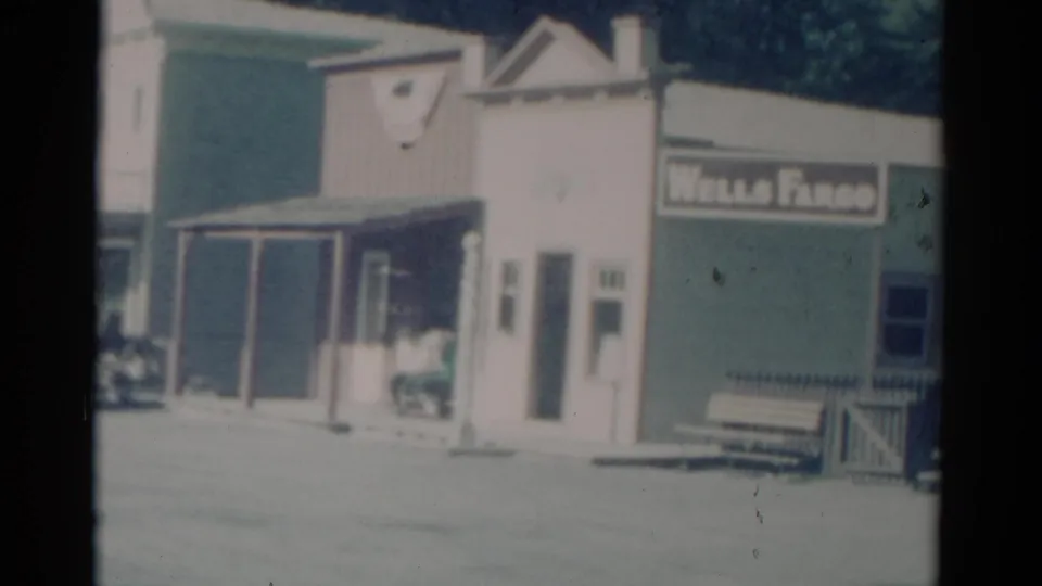 1959 Catskill street frame with a Wells Fargo sign, benches, porch posts, and adjacent shopfronts.