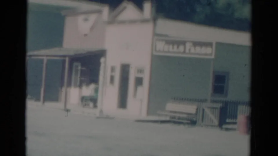 Soft 8mm frame of Catskill storefronts with a Wells Fargo sign, porch railing, bench, and open street area.