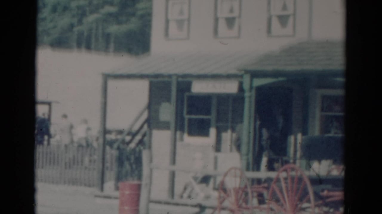 1959 Catskill, New York storefront with green porch posts, red wagon wheels, and people gathered near the entrance.