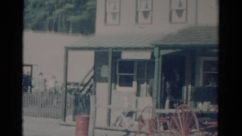 1959 Catskill, New York storefront with green porch posts, red wagon wheels, and people gathered near the entrance.