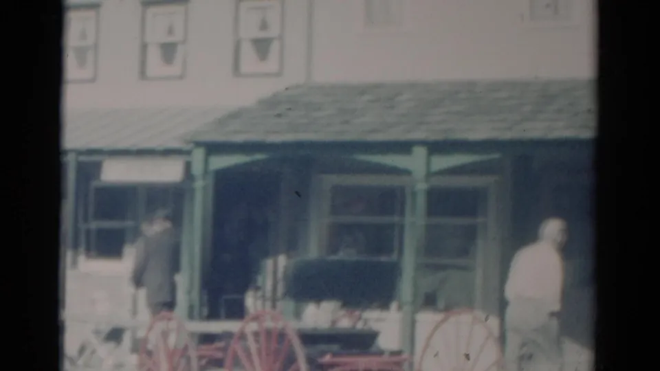 1959 Catskill, New York store exterior with a man in a white shirt at right and wagon wheels near the porch.