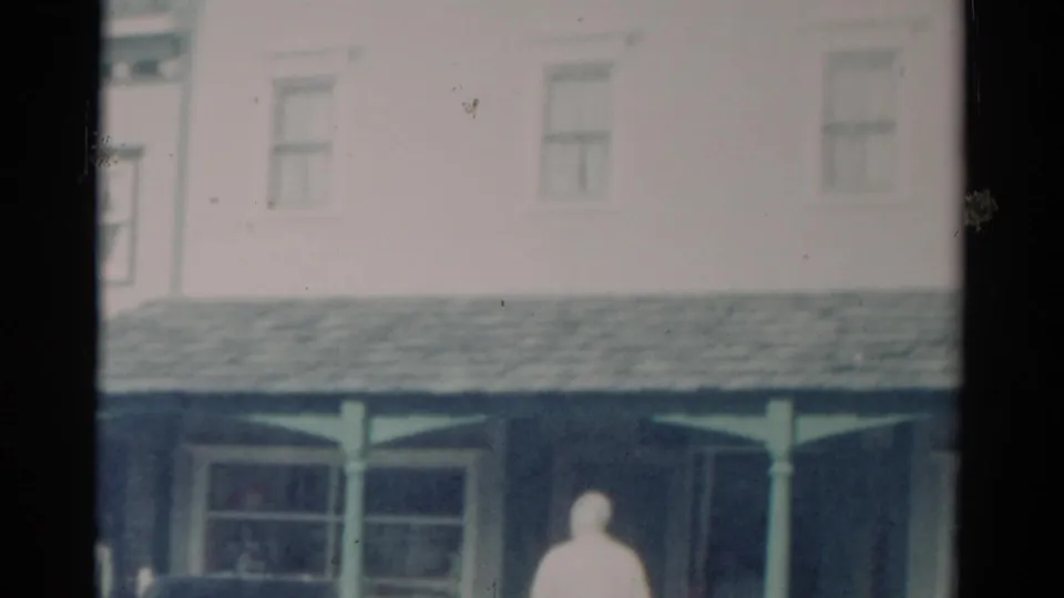 1959 Catskill, New York storefront seen from a closer angle, with upper windows, porch roof, and a person partly visible below.