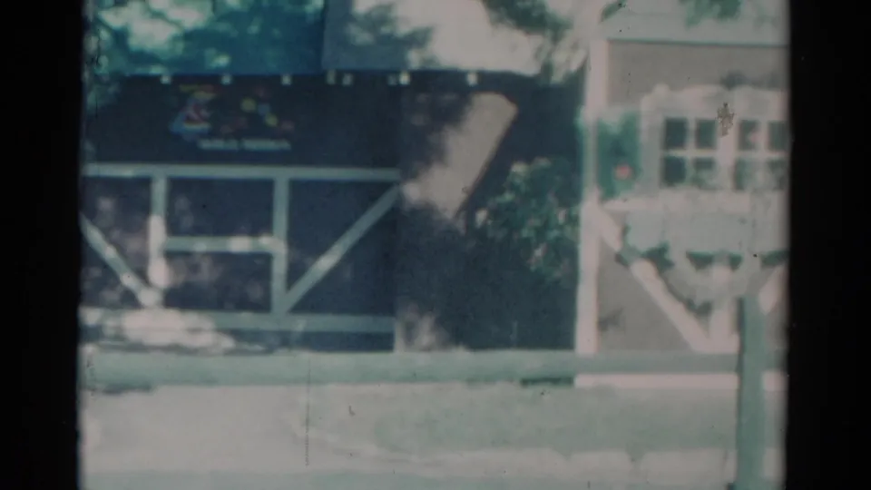 1959 Catskill, New York 8mm frame showing a wood building with white trim, flower boxes, trees, and a roadside foreground.
