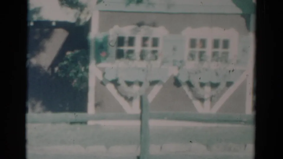 1959 Catskill, New York home-movie frame showing a light wood building with windows and flower boxes beyond a road.