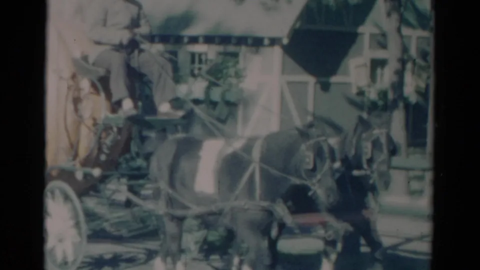 1959 Catskill, New York 8mm frame showing a man seated in a horse-drawn carriage moving past a wood building.