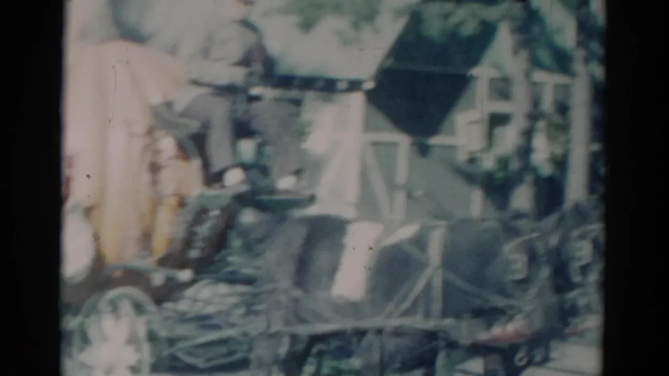 1959 Catskill, New York home-movie frame with a horse-drawn carriage, seated man, and roadside building in soft focus.