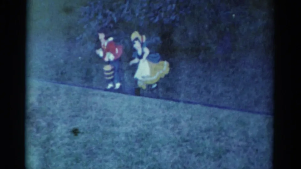 The costumed pair continues across the grass in a soft, blue-tinted 8mm frame from the Catskill home-movie clip.