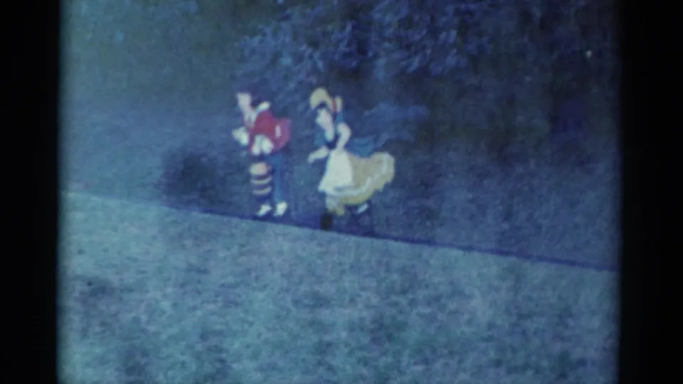 Final 1959 Catskill frame shows the two costumed figures farther along the grassy path, with trees behind and heavy home-movie grain.