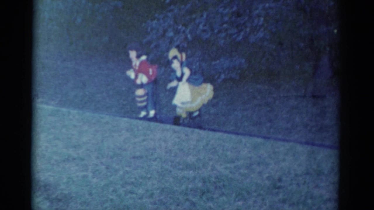 In Catskill, New York, 1959 home-movie footage, two costumed performers move along a grassy path near dark foliage.