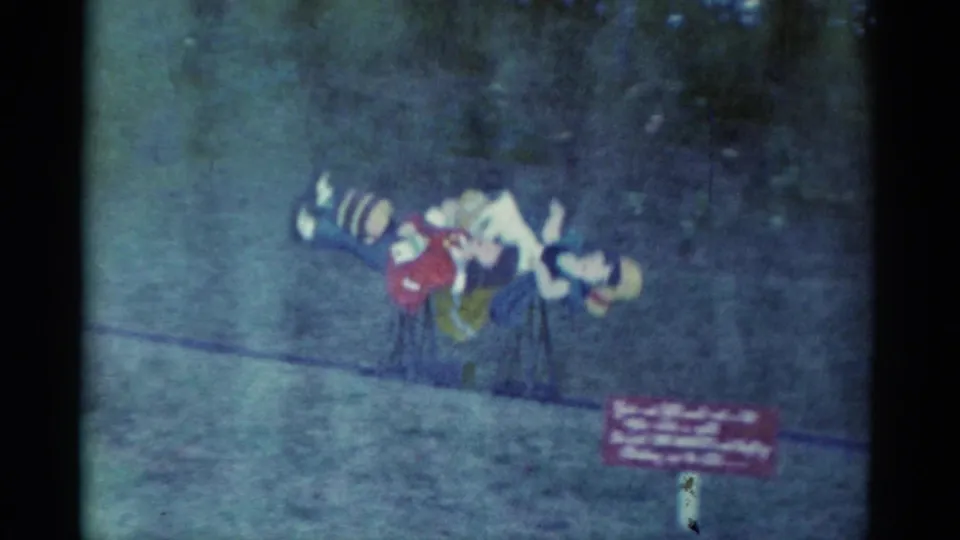 At the end of the 1959 Catskill clip, the costumed figures lean together near the grass path while a small unreadable sign appears in the corner.