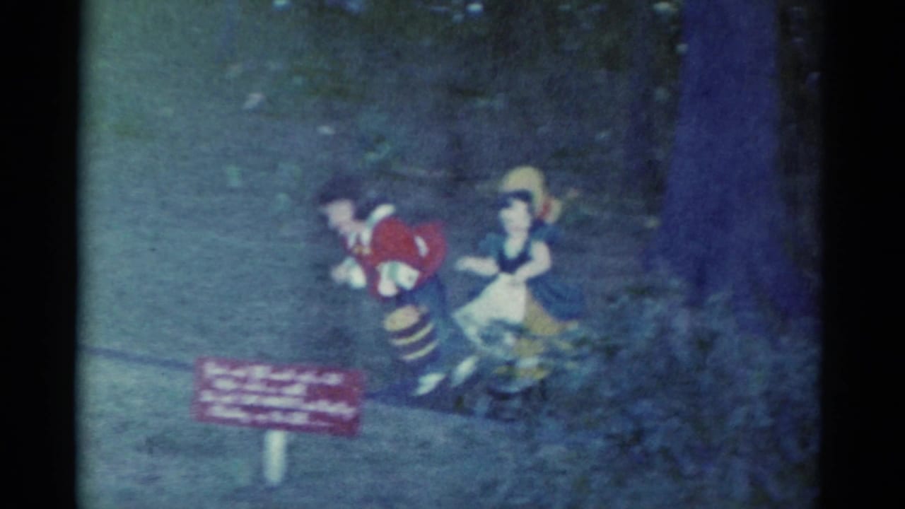 Two puppet or cut-out figures beside a small red sign against a dark outdoor backdrop.