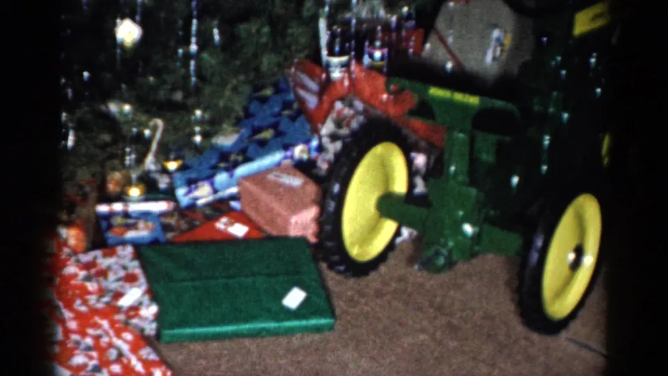 The camera frames a green-and-yellow toy tractor next to wrapped holiday presents beneath the decorated tree in Catskill, New York.