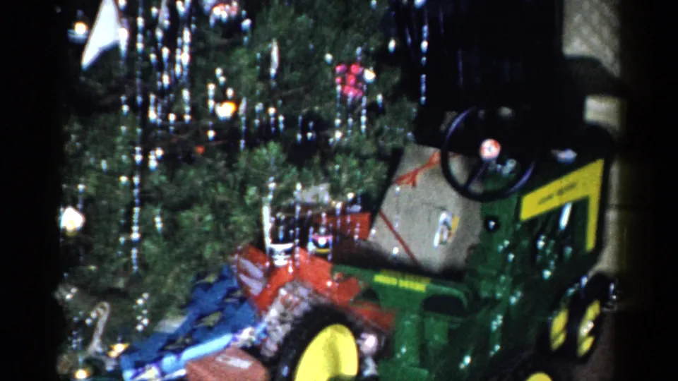 Final frame of the Catskill Christmas scene with the green-and-yellow toy tractor, tinsel-covered tree, ornaments, and holiday parcels.