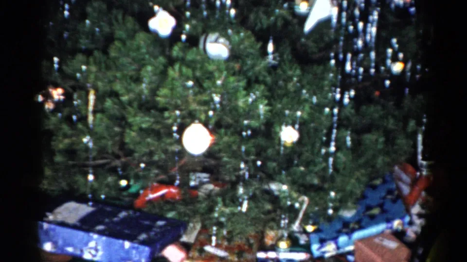 1959 Catskill home-movie view of the tree from another angle, with tinsel, round ornaments, wrapped gifts, and toys visible below.