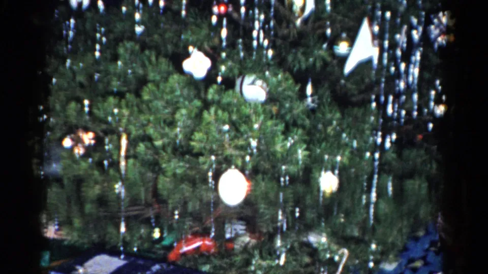 1959 Catskill 8mm frame showing a dense Christmas tree with silver tinsel, white ornaments, and presents partly visible near the floor.