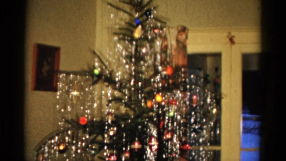 1959 Catskill frame showing the lower portion of a decorated Christmas tree with tinsel, lights, ornaments, wall picture, and doorway.