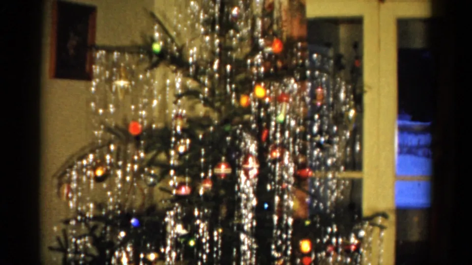 1959 Catskill home interior frame with a Christmas tree, dense silver tinsel, colored ornaments, lights, and pale window or door frames.