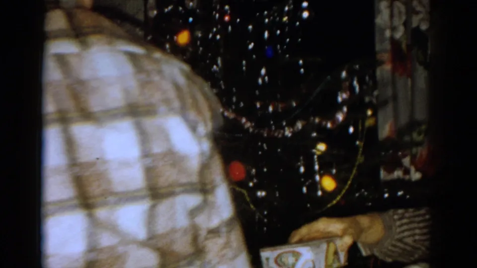 1959 Catskill frame with a close partial view of a plaid-shirted person beside a decorated Christmas tree and visible gifts.