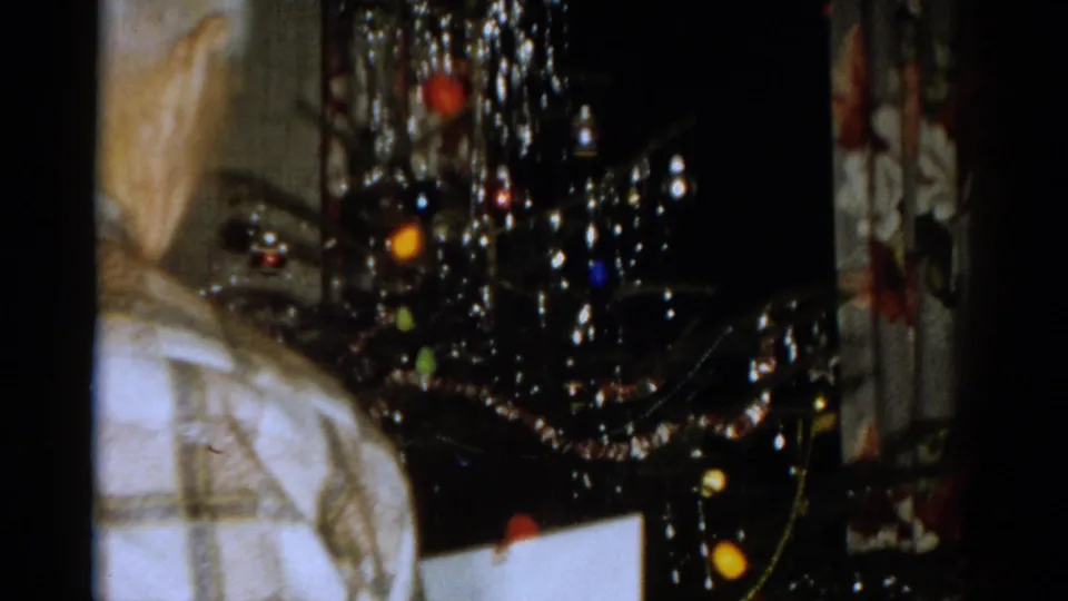 The camera frames the 1959 living-room Christmas tree, with tinsel, ornaments, and part of a plaid-shirted person at the edge.