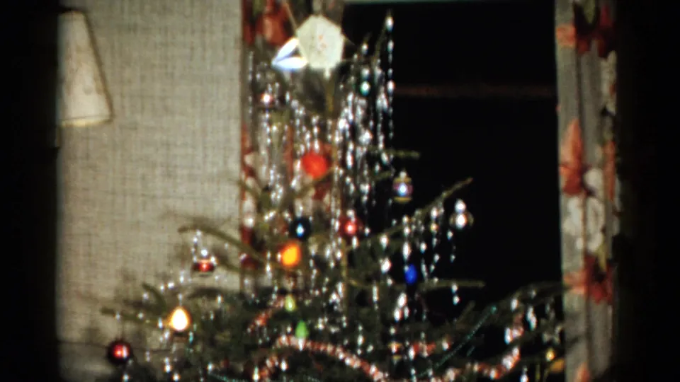 A decorated Christmas tree fills the frame, showing tinsel, colored ornaments, lights, and the living-room wall in Catskill, New York.